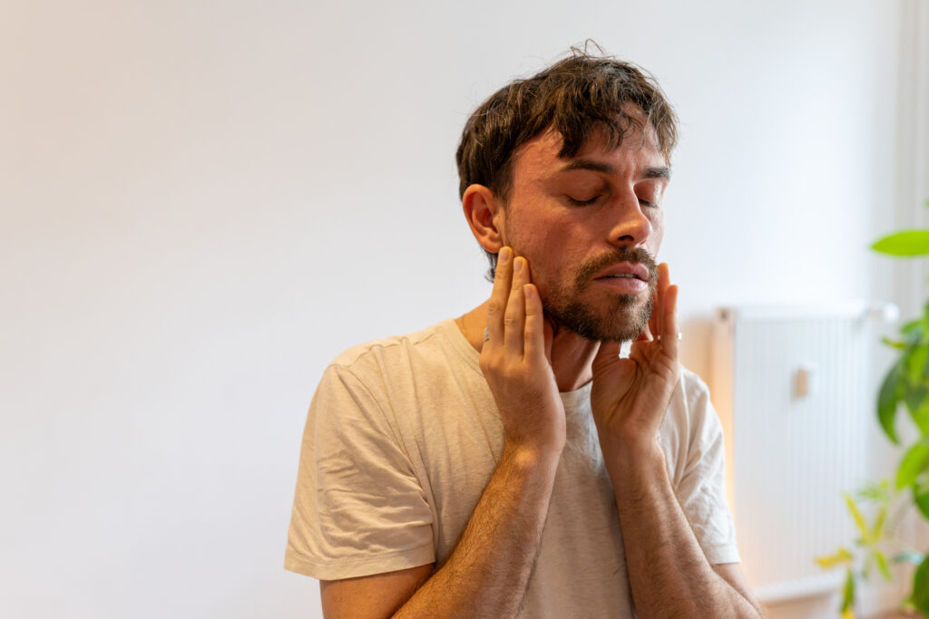 Kieferschmerzen und Zähneknirschen: Mann hält sich den verspannten Kiefer – Osteopathie bei Harald Erb, Berlin Prenzlauer Berg