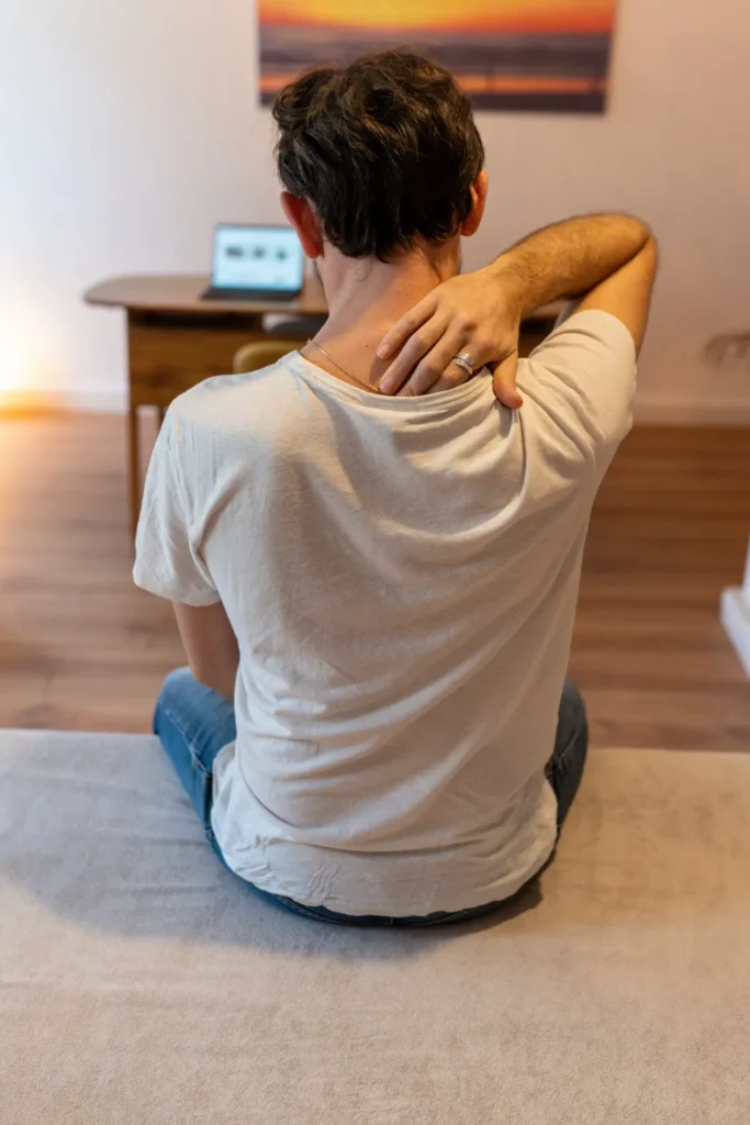 Schmerzen zwischen den Schulterblättern: Patient greift an den verspannten oberen Rücken – Osteopathie bei Harald Erb, Berlin Prenzlauer Berg